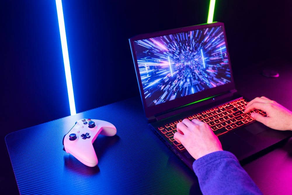 Cómo encontrar una laptop gamer que sí cumpla tus expectativas 20 Mujer joven con auriculares y gafas de sol usando una laptop gamer en un entorno de iluminación neón vibrante.