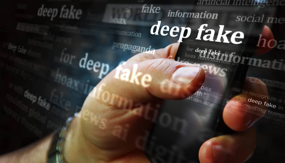 Phishing con Inteligencia Artificial: Cómo están cambiando las Ciberamenazas 22 Mano sujetando un teléfono mostrando la palabra "deepfake" rodeada de términos relacionados con noticias falsas e IA. Ejemplo de un ataque deepfake.