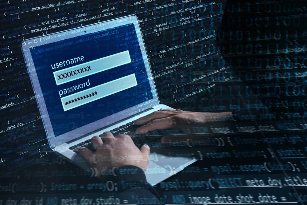 Concepto de ciberseguridad con un hacker intentando ataques de contraseñas en un portátil con código binario de fondo.