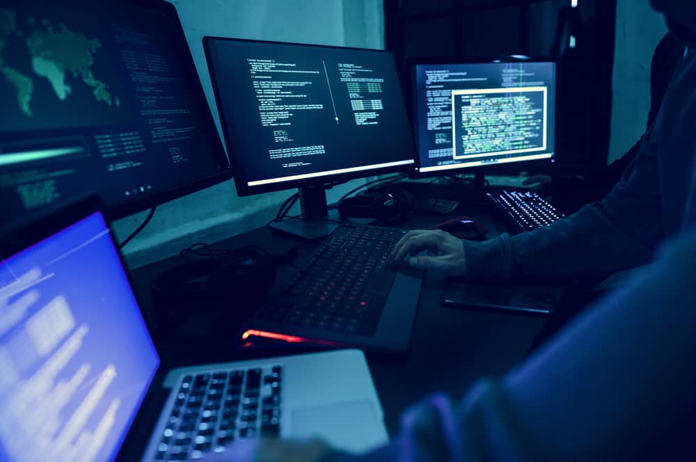 Hacker ético trabajando en varias pantallas con código, demostrando las habilidades clave necesarias para la ciberseguridad.