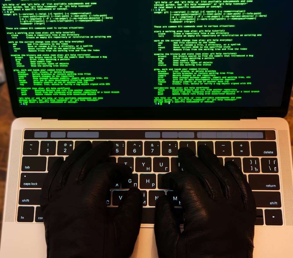 Persona con guantes negros escribiendo código en un portátil, ilustrando la ejecución de ataques a aplicaciones web.
