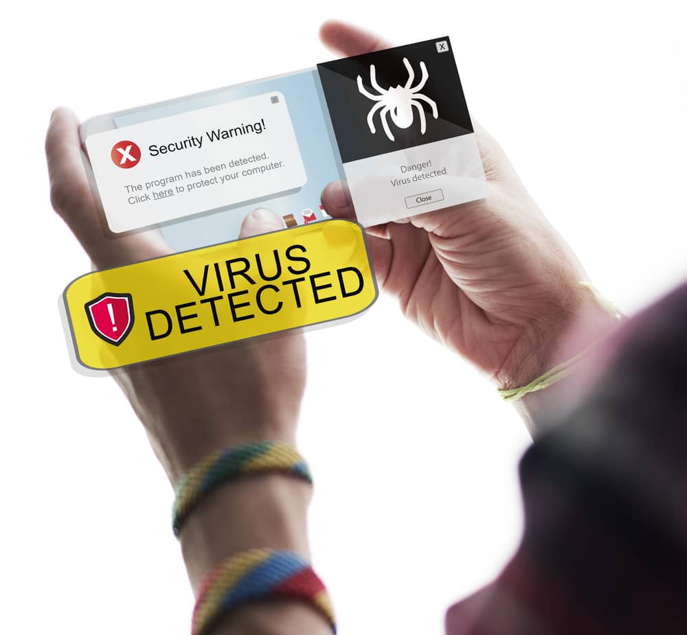Manos sosteniendo un smartphone transparente con varias alertas de seguridad y advertencias de virus detectado en la pantalla.