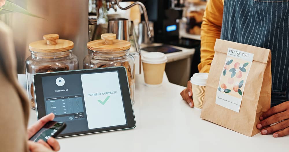 Sostenibilidad digital: tecnología verde en restauración 20 Un cliente paga con su móvil en una cafetería, un ejemplo de la sostenibilidad en terminales TPV que agilizan la venta.